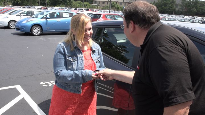 a man giving a key to a woman next to a vehicle
