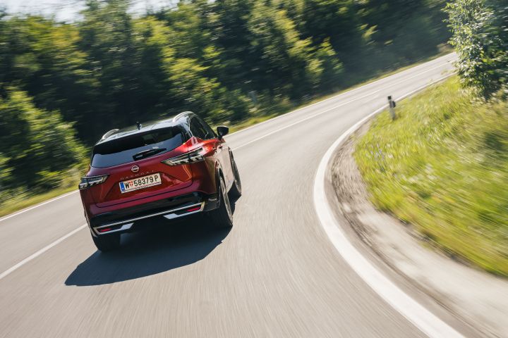 Heckansicht eines Nissan Qashqai in Fuji Sunset Red, der eine Landstraßenkurve durchfährt