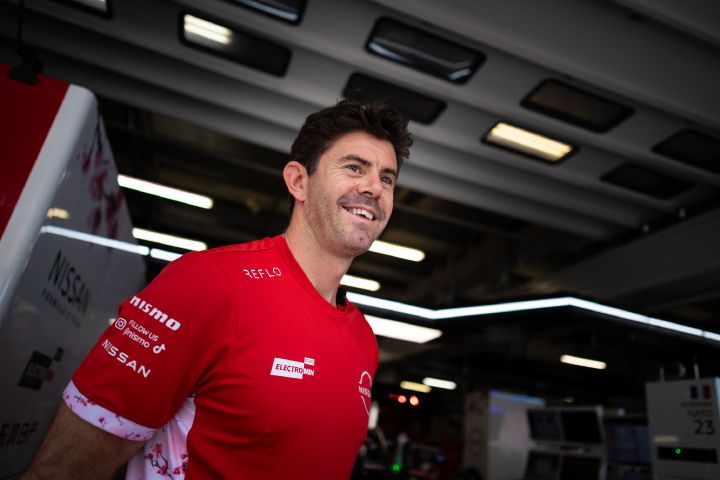 Norman Nato steht lächelnd in seinem roten Team-T-Shirt in der Teamgarage.