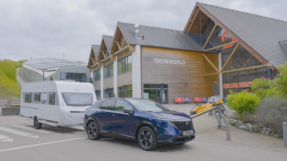 Nissan ARIYA tirant une caravane, garé devant la piste de ski indoor 'Snowworld'
