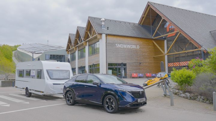 Nissan ARIYA tirant une caravane, garé devant la piste de ski indoor 'Snowworld'