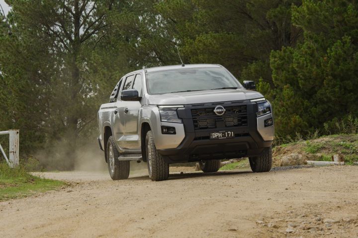 2026 Nissan Navara ST dual cab ute finished in Summit Silver shown navigating a dirt incline from the front three-quarter angle in a bush setting.