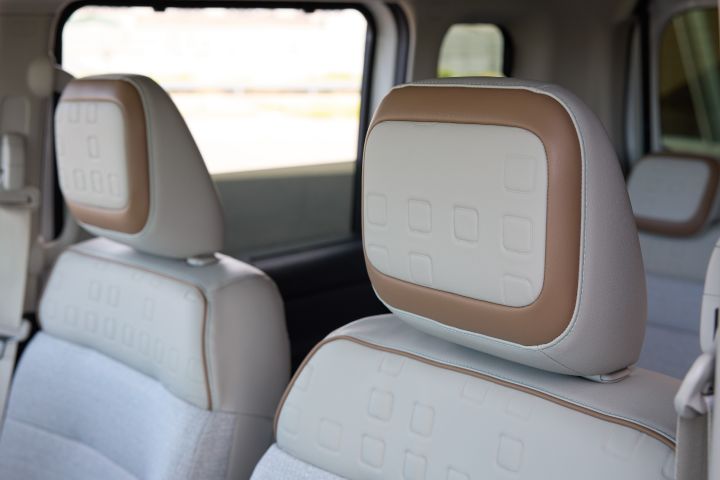 Interior view of the new Nissan Roox kei car. The front seat headrests feature a beige and brown two-tone design, with outdoor scenery visible through the car windows in the background.
