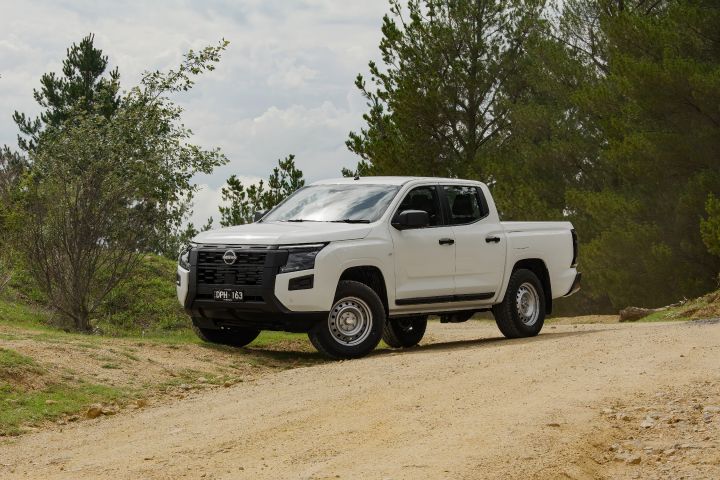 2026 Nissan Navara SL dual cab ute finished in Alpine White shown from the front-left on a gravel road, featuring the black grille, side step and steel-wheel setup.