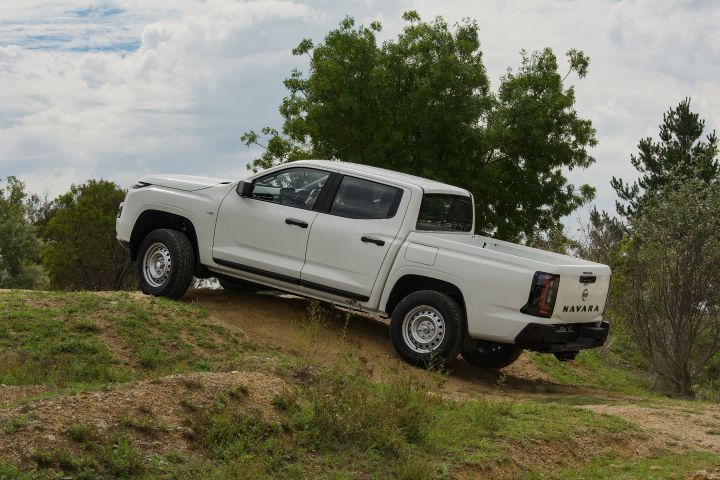 2026 Nissan Navara SL dual cab ute finished in Alpine White descending a dirt bank from the rear-left angle, showing the side step, tray panels and tail-light design