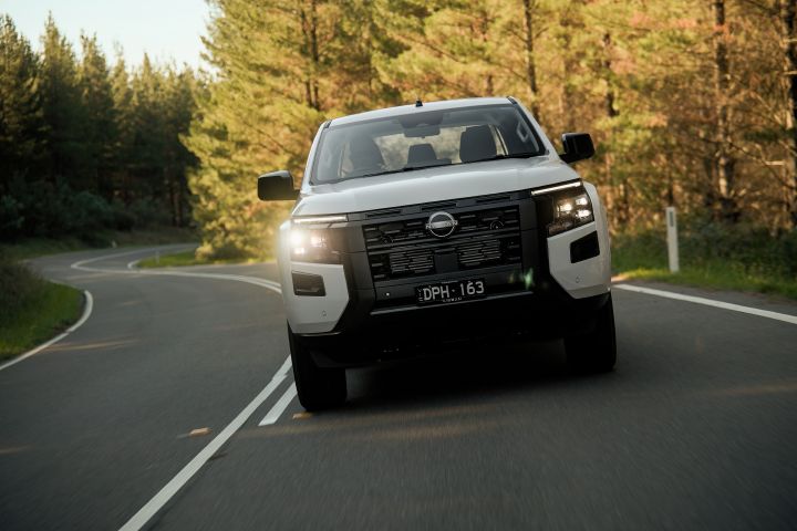 2026 Nissan Navara SL dual cab ute finished in Alpine White photographed head-on while driving through a forested bend, with the front lighting and grille clearly visible.