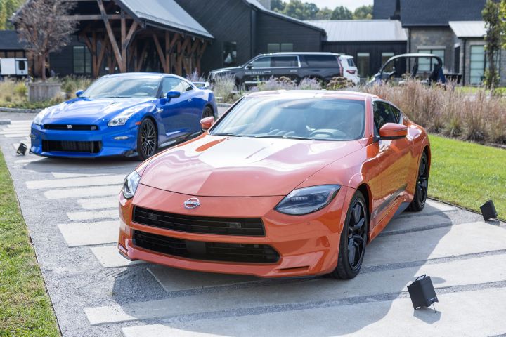 An orange Nissan Z and blue Nissan GT‑R parked on cement in front of a large black venue building