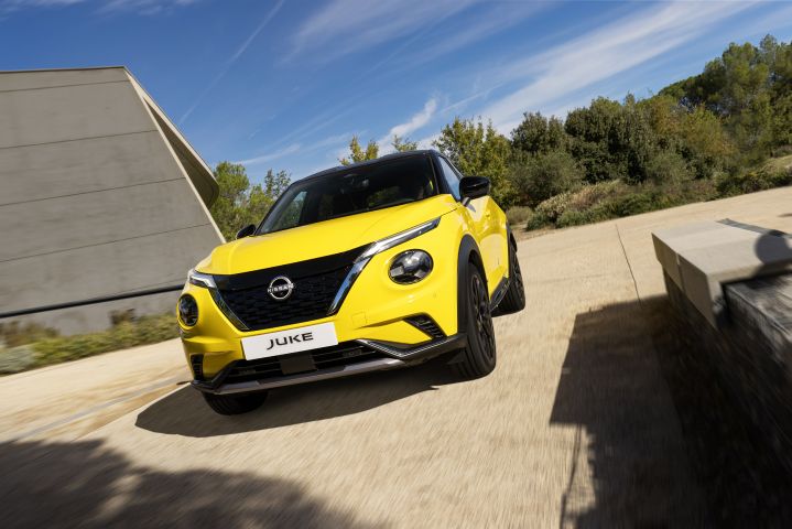 Fahraufnahme gelber Nissan Juke auf hellem Untergrund vor hellem Haus und Wiese