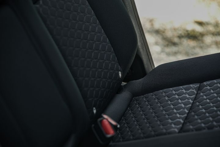 Tight seat close-up highlighting the patterned cloth upholstery, side bolsters, seatbelt latch and stitching on the front seating surface.