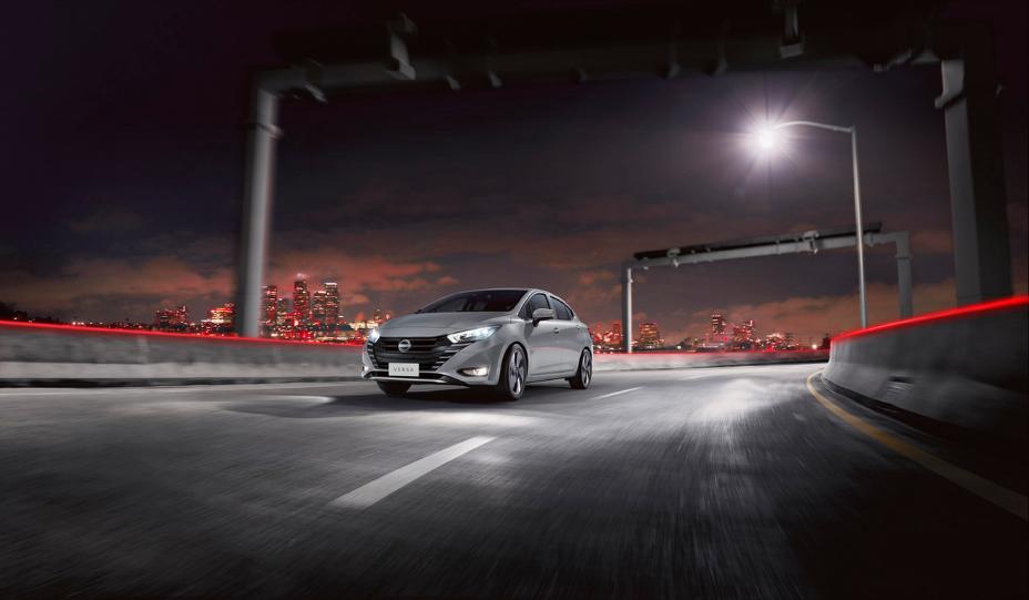 Auto Nissan en carretera a gran velocidad de noche, con una ciudad de fondo con luces rojas