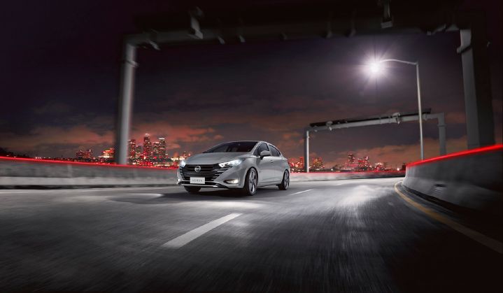 Auto Nissan en carretera a gran velocidad de noche, con una ciudad de fondo con luces rojas