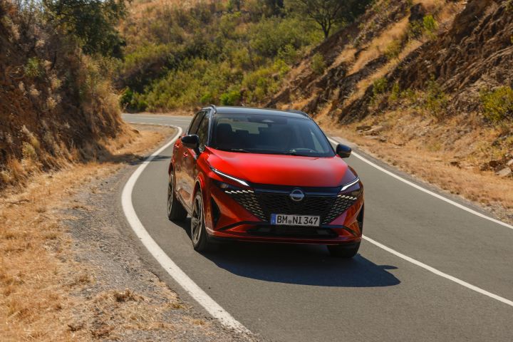 Nieuwe Nissan Qashqai in de kleur Fuji Sunset Red, van de voorzijde gezien, rijdend op een  weg in Portugal