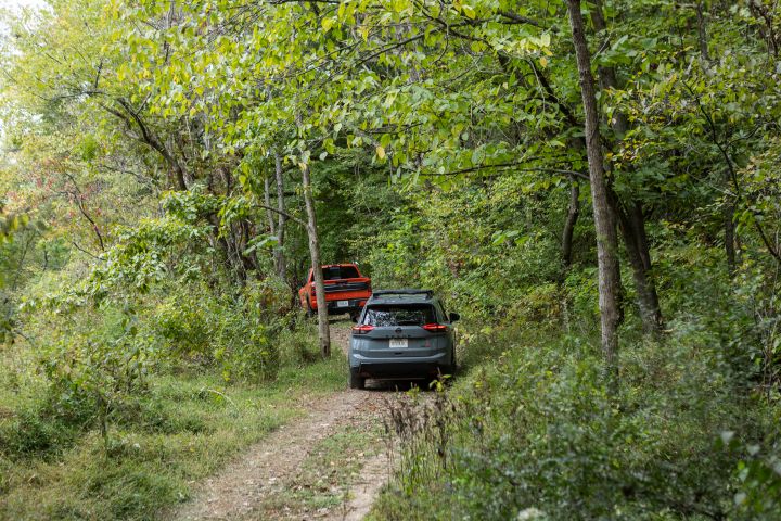 A Nissan crossover and truck heading down a path in the woods, you only see the rear of the cars.