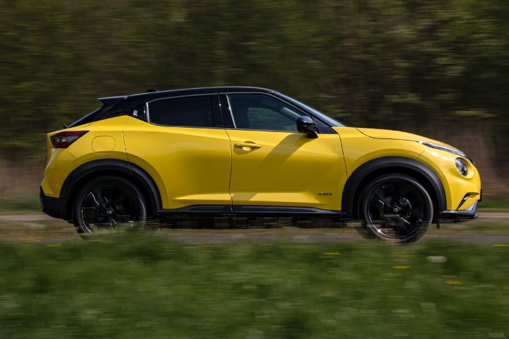 Jadący żółty Nissan Juke (widok z boku) na tle zieleni