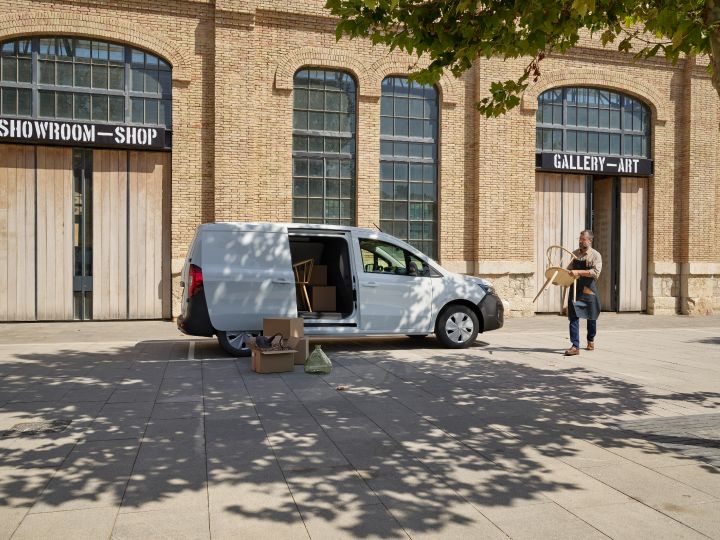 Vue latérale d’un Nissan Townstar EV Fourgon L2 blanc chargé avec des cartons et du matériel. Un homme tenant une chaise marche en direction du véhicule.