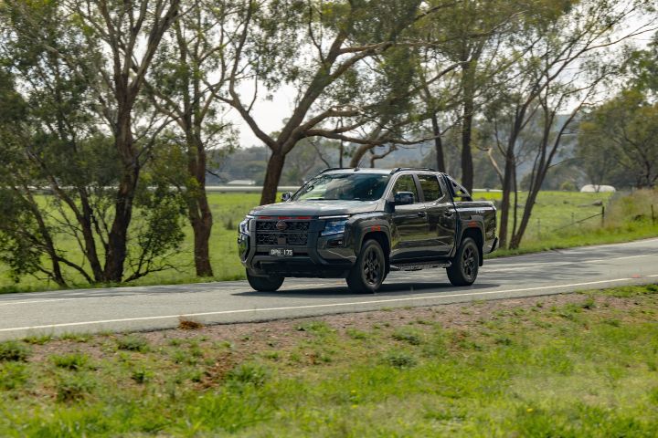 2026 Nissan Navara PRO-4X finished in Boulder Grey captured in a telephoto roadside image travelling past mature trees and green paddocks.