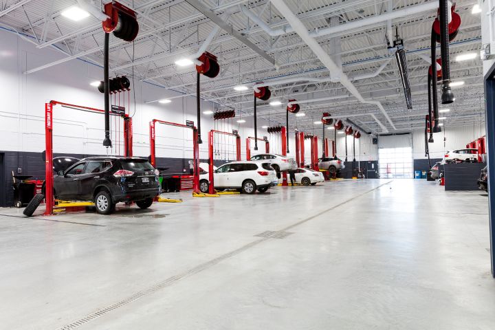 Atelier de réparation automobile moderne avec plusieurs véhicules sur des ascenseurs hydrauliques rouges et des outils suspendus au plafond.