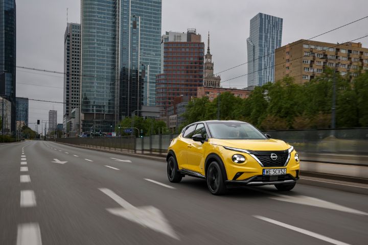 Jadący żółty Nissan Juke (widok z półprofilu) z budynkami w tle