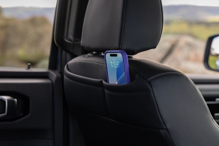 Rear cabin view of a 2026 Nissan Navara ST-X showing the back of a front seat with a smartphone placed in the seatback pocket, with the rear door trim and blurred countryside visible through the side window.