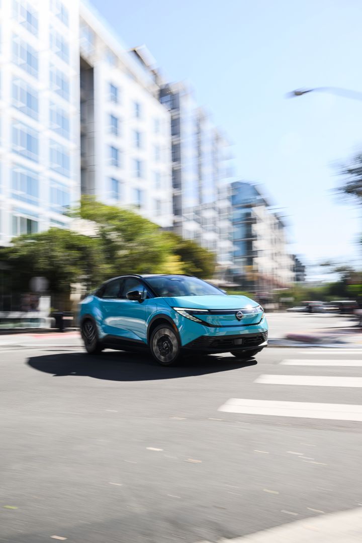The 2026 Nissan LEAF making a turn on a city street, the buildings are blurred to imply motion.