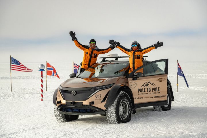 Zwei Personen in orangefarbenen Overalls stehen neben dem Nissan Pole-to-Pole-Fahrzeug im Schnee