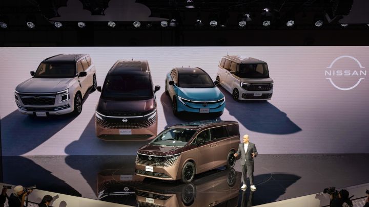 On the stage, the all-new Elgrand in Fuji Dawn and Shigoku two-tone colors is positioned diagonally, facing slightly to the left.  Next to the vehicle stands CEO Ivan Espinosa in a suit, with hands clasped in front. In the background, four models—Elgrand, Patrol, Nissan LEAF, and Roox—are displayed.