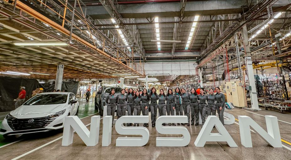 Grupo de 14 mujeres colaboradoras de Planta, luciendo su uniforme, Sentra blanco, letras volumétricas blancas Nissan. Y de fondo la planta de manufactura.
