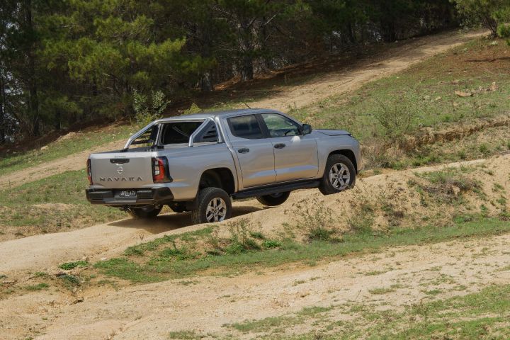 2026 Nissan Navara ST dual cab ute finished in Summit Silver captured from the rear-left as it crests a dirt rise.