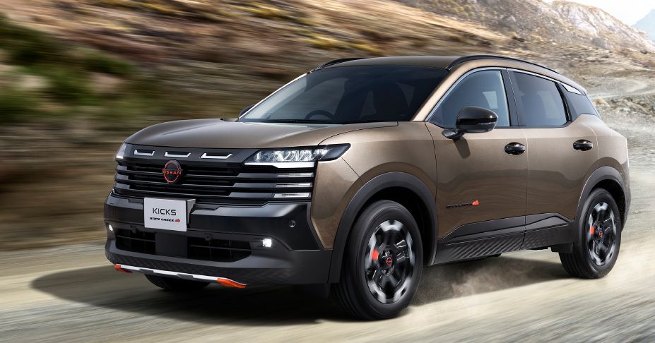 A beige-toned kicks rock creek is driving on an unpaved road in a front three-quarter view facing right. The black-accented grille and wheels, along with lava red accent parts, convey a strong and adventurous character. Dust rises around the rotating tires as the vehicle moves. The background features a rugged mountainous landscape with exposed rock faces, while a panning effect blurs the rocks and ground horizontally, emphasizing motion. The scene highlights both the vehicle's suv toughness and its active driving performance.