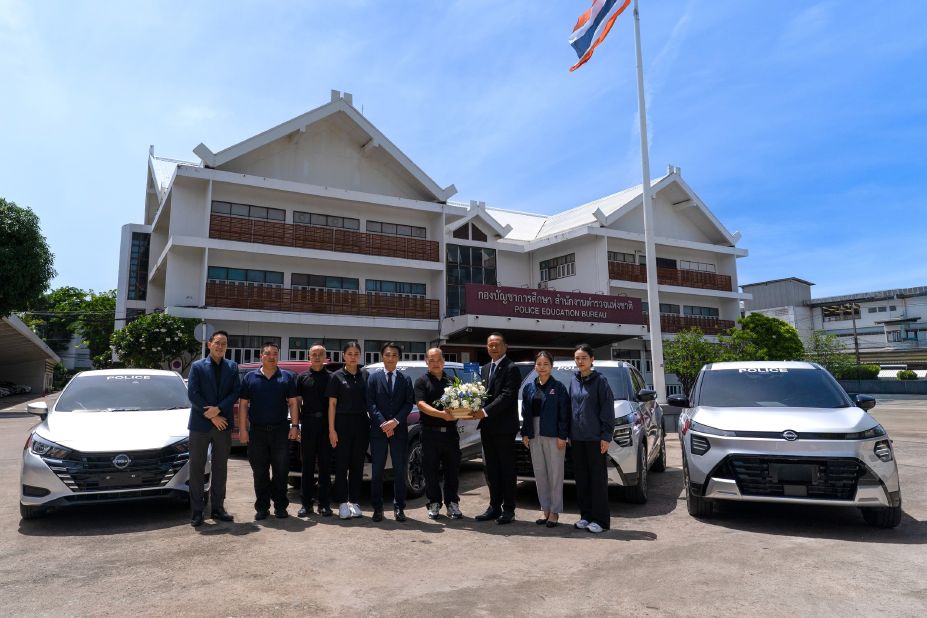 Group photo in front of an office building with Nissan vehicles parked on both sides.
