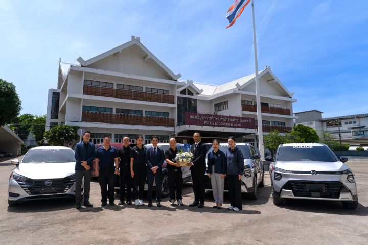 Group photo in front of an office building with Nissan vehicles parked on both sides.