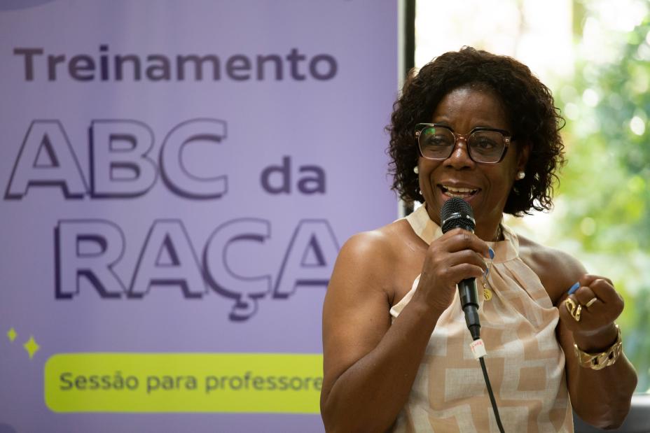 Mulher negra segura o microfone em frente ao cartaz ‘Treinamento ABC da Raça’