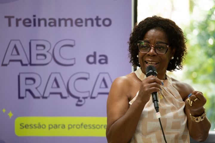 Mulher negra segura o microfone em frente ao cartaz ‘Treinamento ABC da Raça’