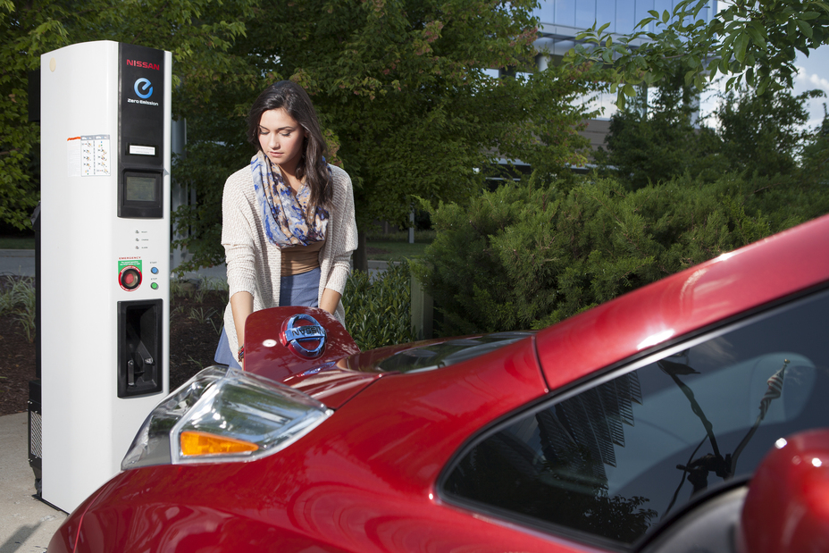 A lady utilizing a charging station to recharge her electric 2013 Nissan LEAF