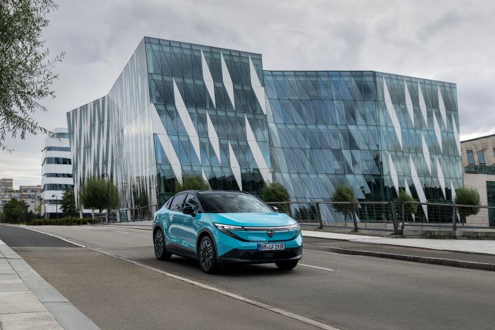 3/4-Frontaufnahme eines türkisen Nissan LEAF, der über eine urbane Straße vor modernen Hochhäusern fährt