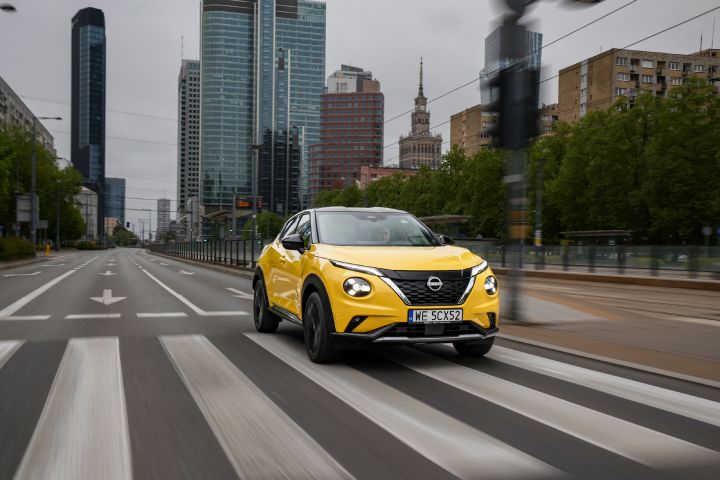 Jadący żółty Nissan Juke (widok z półprofilu) z budynkami w tle