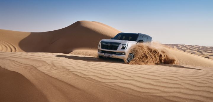 The Patrol is driving over desert dunes, demonstrating its powerful off-road capabilities in harsh terrain.