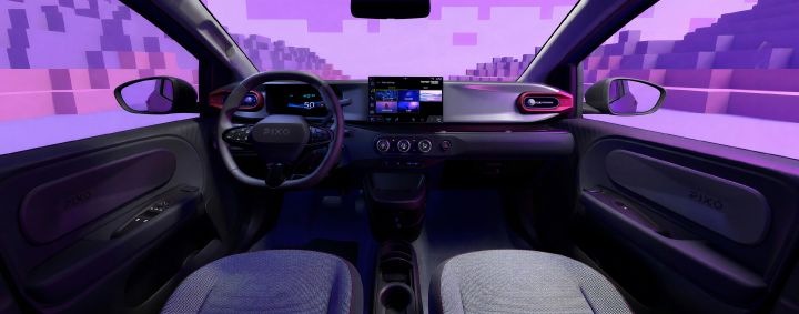 Photograph showing compact-car interior, highlighting dashboard design and driver controls. Purple ambient lighting, digital instrument cluster, central touchscreen, steering wheel, side mirrors, textured front seats, and pixel-like cityscape visible through windshield.