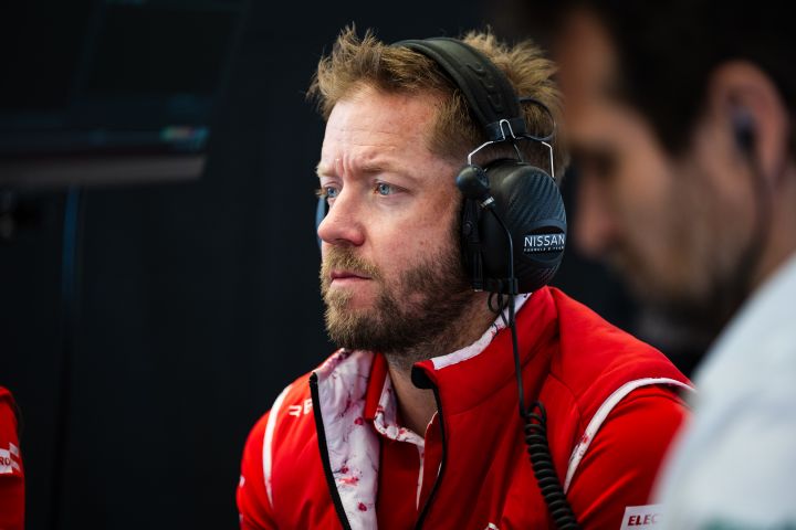 Sam Bird schaut zu, bekleidet mit der Ausrüstung des Nissan-Formel-E-Teams und mit Kopfhörern.