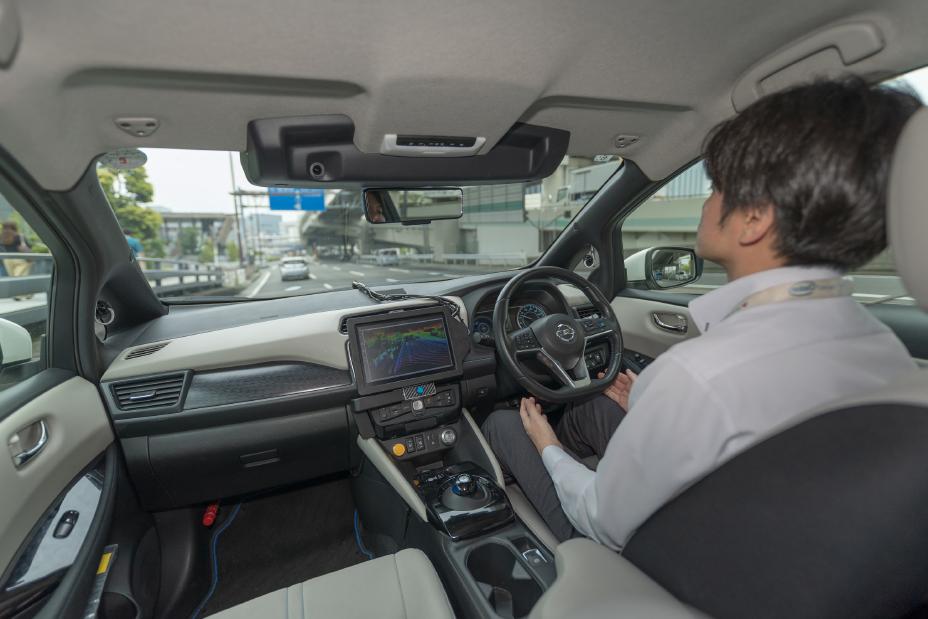 Innenraum des autonom fahrenden Nissan, der Fahrer hat die Hände nicht am Lenkrad und das Auto fährt über öffentliche japanische Straßen
