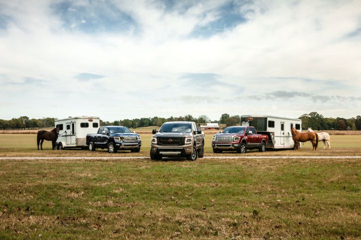 Three Nissan TITANs parked in a field with trailers and horses.