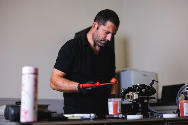Ein Mechaniker gibt eine rote Masse mit einem Spatel auf ein Bauteil des Nissan Formel E Rennwagens