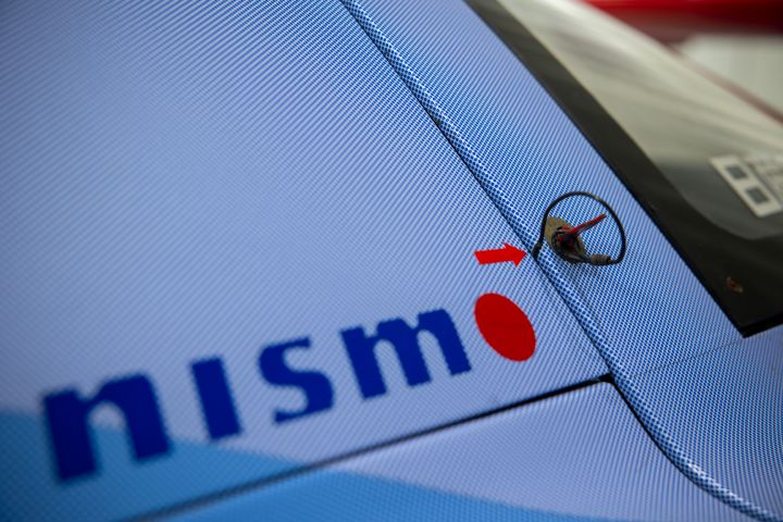 A close-up of a NISMO logo on a blue Nissan R390 GT1 Le Mans race car shown within the Nissan global gallery in Yokohama, Japan.