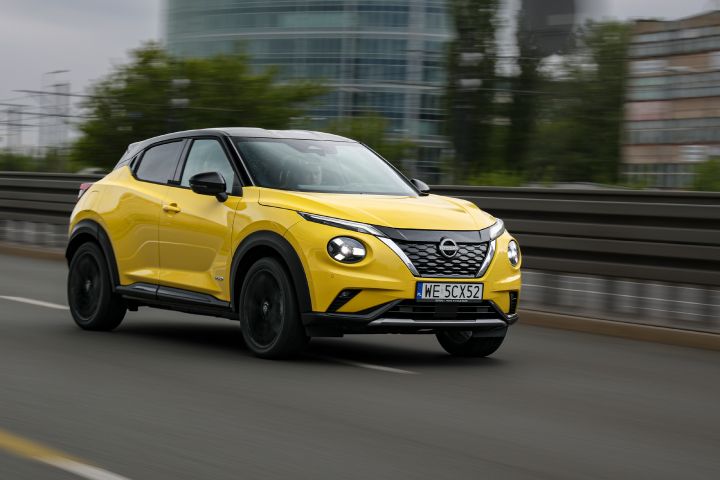 Jadący żółty Nissan Juke (widok z półprofilu) z budynkami w tle