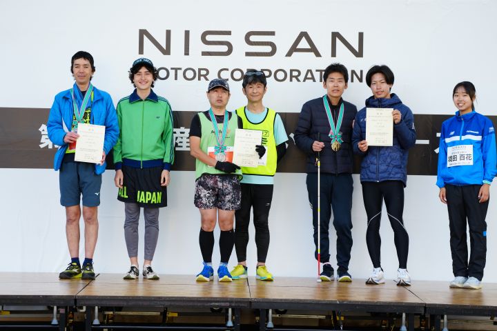 3人の選手と各伴走者が舞台上で表彰されている様子