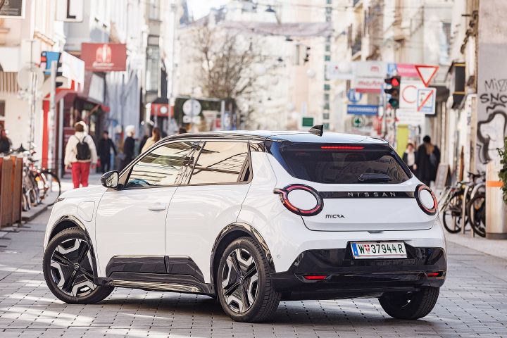 3/4 Heckansicht eines weißen Nissan Micra mit schwarzem Kontrastdach, das Auto steht in einer belebten Fußgängerzone