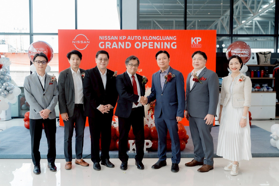 ภาพกลุ่มผู้บริหารยืนบนเวทีจับมือกันในงานเปิดตัว Nissan KP Auto Klongluang โดยมีฉากหลังสีแดงและป้ายแบรนด์ภายในโชว์รูม