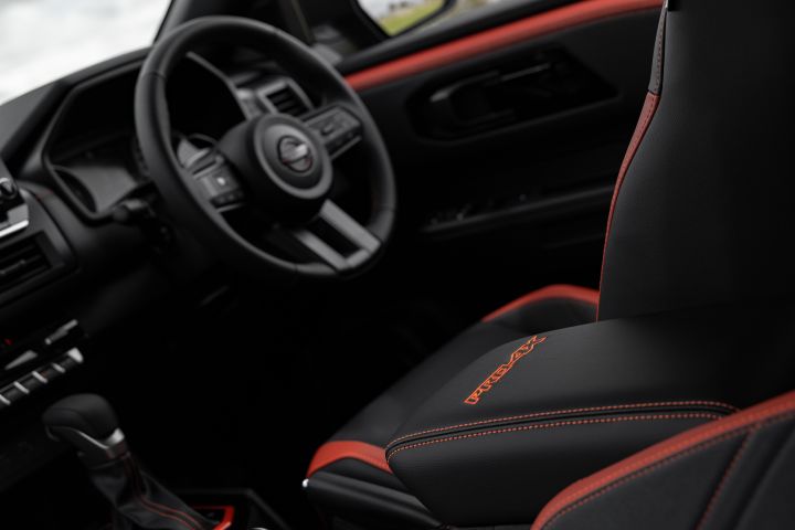 2026 Nissan Navara PRO-4X finished in Boulder Grey showing an over-shoulder cabin view with embroidered armrest, steering wheel, gear selector and red door garnish.