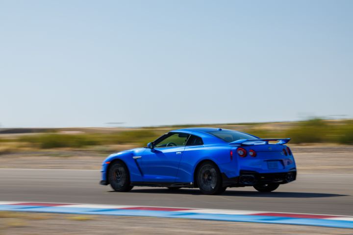 Slightly blurry motion image of the profile of 2024 GT‑R Special Edition being driven on a race track with blue sky