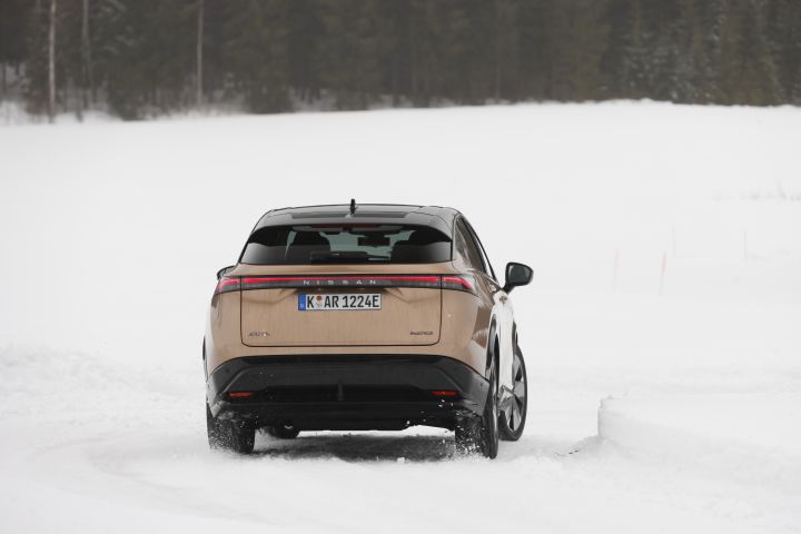 Elektroauto Nissan Ariya e‑4ORCE in Akatsuki Copper mit Dach und Außenspiegel in Pearl Black fährt auf Schnee